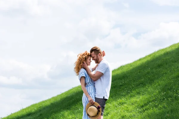 Вид сбоку счастливой рыжеволосой пары, стоящей лицом к лицу на зеленом холме — стоковое фото