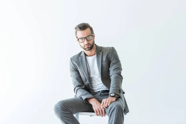 Hombre de negocios con estilo en traje gris sentado en la silla, aislado en blanco - foto de stock