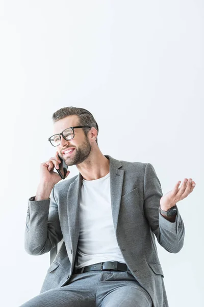 Hombre de negocios guapo en traje gris haciendo gestos y hablando en el teléfono inteligente, aislado en blanco - foto de stock