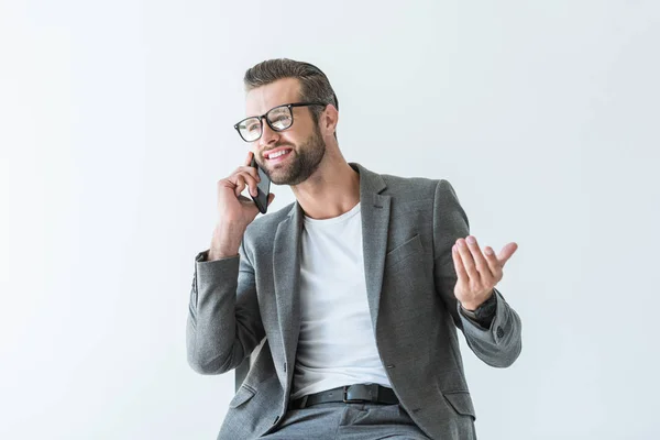 Hombre de negocios sonriente en chaqueta gris gesticulando y hablando en el teléfono inteligente, aislado en blanco - foto de stock