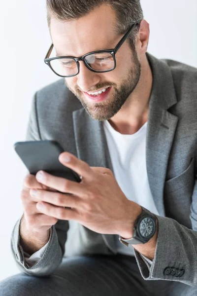 Счастливый бородатый человек в серой куртке с помощью смартфона, изолированные на белом — стоковое фото