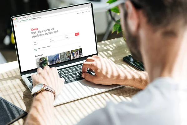 Back view of man using laptop with airbnb website on screen — Stock Photo