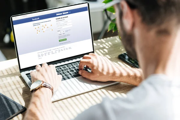 Partial view of man using laptop with facebook website on screen — Stock Photo