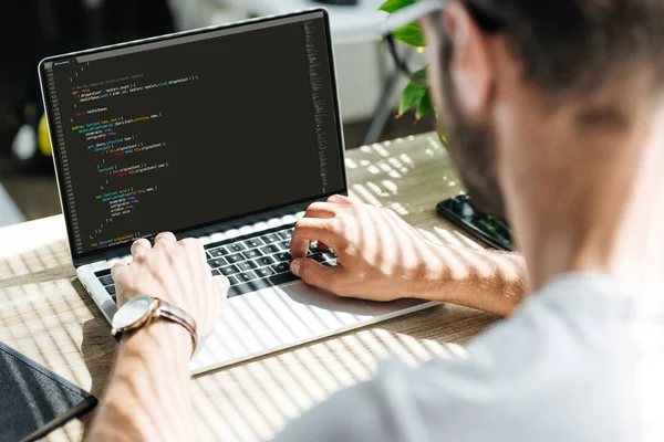 Back view of man using laptop with html code on screen — Stock Photo