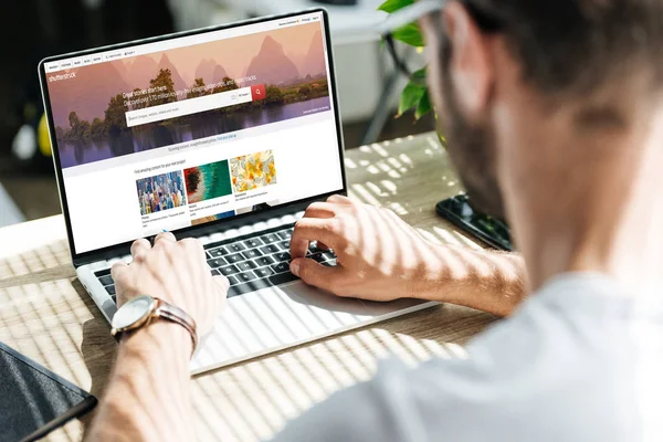 Back view of man using laptop with shutterstock website on screen — Stock Photo