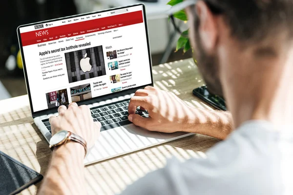 Vista parcial del hombre usando el ordenador portátil con el sitio web de noticias de la BBC en la pantalla - foto de stock