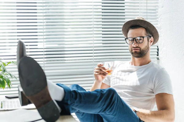 Stylish bearded man in hat holding glass of whiskey — Stock Photo