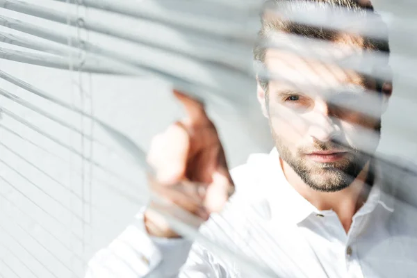 Homme sérieux regardant par la fenêtre jalousie, foyer sélectif — Photo de stock