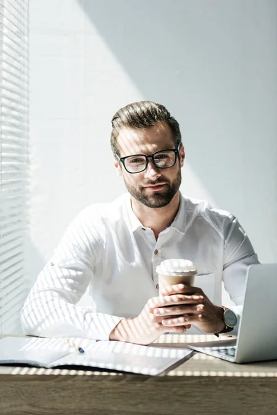 Bel homme d'affaires assis sur le lieu de travail avec ordinateur portable, paperasse et tasse de café — Photo de stock