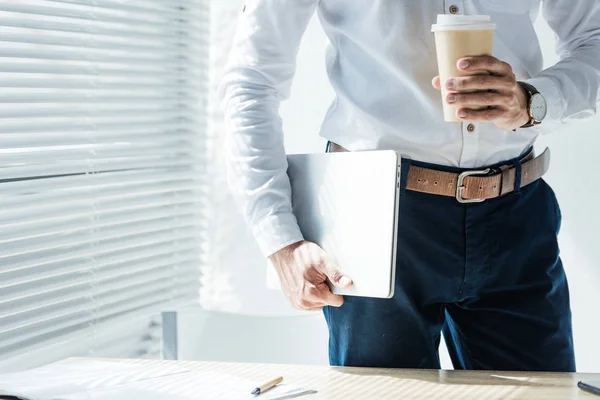 Cropped view of businessman holding laptop and coffee to go — Stock Photo