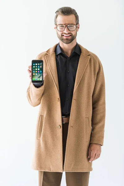 Barbudo sonriente hombre en abrigo presentando iphone, aislado en blanco - foto de stock