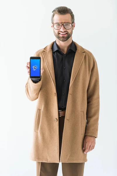 Stylish man in eyeglasses and coat presenting smartphone with shazam appliance, isolated on white — Stock Photo