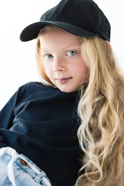Портрет красивої дитини з довгим кучерявим волоссям у чорній футболці та кепці, дивлячись на камеру ізольовано на білому — стокове фото