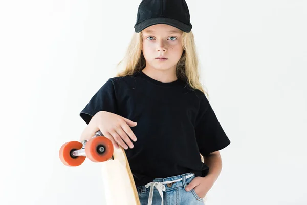 Entzückendes Kind mit langen lockigen Haaren, das am Skateboard lehnt und isoliert auf weiß in die Kamera schaut — Stockfoto