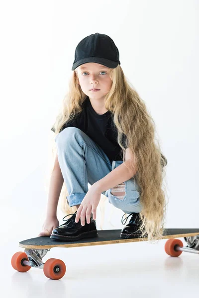 Beautiful child with long curly hair crouching on skateboard and looking at camera on white — Stock Photo