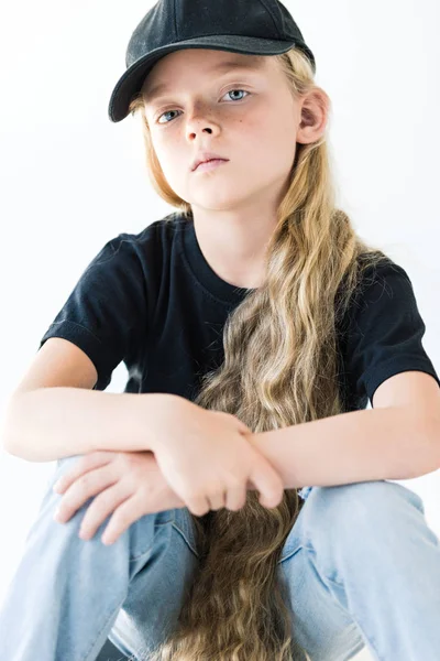 Retrato de un hermoso niño con el pelo largo y rizado con gorra negra y mirando a la cámara aislada en blanco - foto de stock