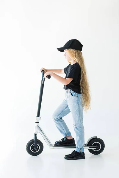 Vista laterale del bambino con lunghi capelli ricci equitazione scooter isolato su bianco — Foto stock