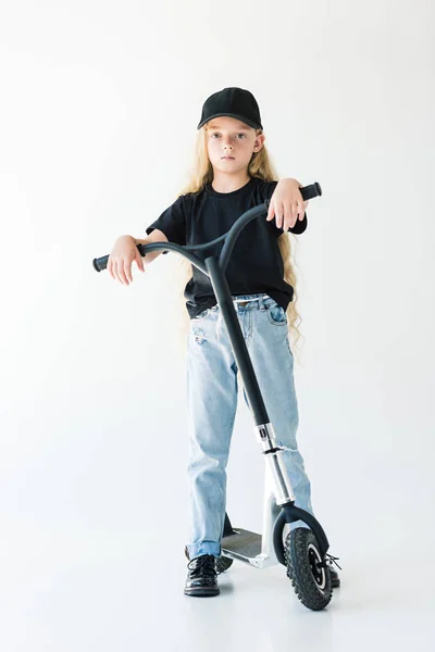 Vista completa del niño con el pelo largo y rizado de pie con scooter y mirando a la cámara aislada en blanco - foto de stock