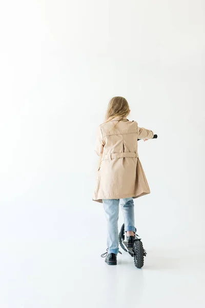 Vista posteriore del bambino in trench equitazione scooter isolato su bianco — Foto stock