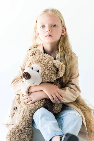 Adorable niño con pelo largo rizado sosteniendo osito de peluche y mirando a la cámara aislada en blanco - foto de stock