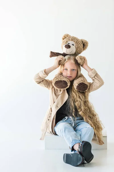 Beautiful stylish kid holding teddy bear and looking at camera isolated on white — Stock Photo