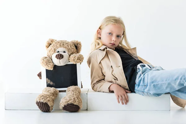 Teddybär mit digitalem Tablet und entzückendem stilvollem Kind, das in die Kamera auf weiß schaut — Stockfoto