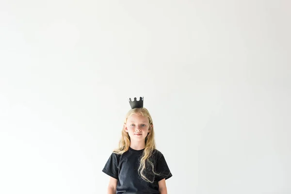 Adorable niño con largo rizado escuchar vistiendo corona negra y sonriendo a la cámara aislado en blanco - foto de stock