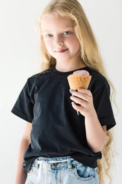 Очаровательный ребенок в черной футболке ест мороженое и улыбается в камеру, изолированную на белом — стоковое фото