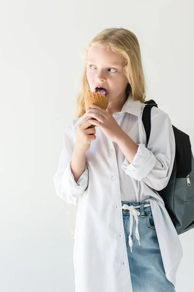 Beautiful kid with backpack eating ice cream and looking away isolated on white — Stock Photo