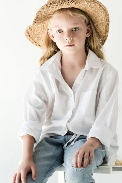 Retrato de niño hermoso en sombrero de mimbre sentado y mirando a la cámara en blanco - foto de stock