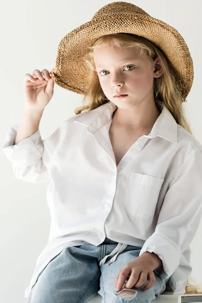 Hermoso niño pequeño en sombrero de paja sentado y mirando a la cámara en blanco - foto de stock