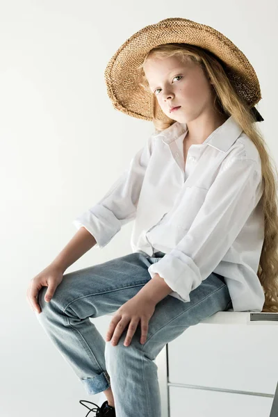 Bellissimo bambino in cappello di vimini seduto e guardando la fotocamera su bianco — Foto stock