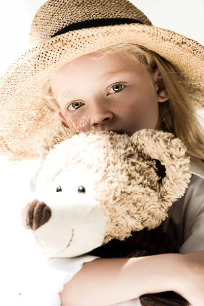 Adorable child in wicker hat holding teddy bear and looking at camera on white — Stock Photo