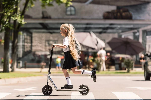 Side view of cute little child with long curly hair riding scooter on street — Stock Photo