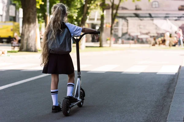 Back view of cute little child with backpack riding scooter on street — Stock Photo