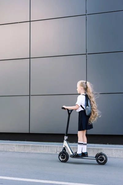 Adorable petite écolière avec de longs cheveux bouclés équitation scooter sur la rue — Photo de stock