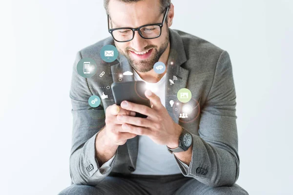 Homme d'affaires souriant en costume gris en utilisant smartphone, isolé sur blanc avec des icônes — Photo de stock