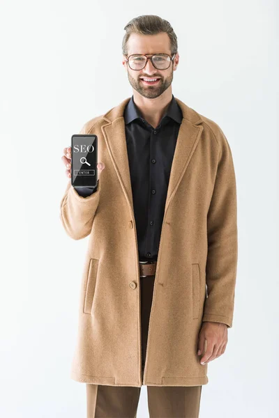 Desarrollador sonriente barbudo presentando smartphone con búsqueda SEO, aislado en blanco - foto de stock