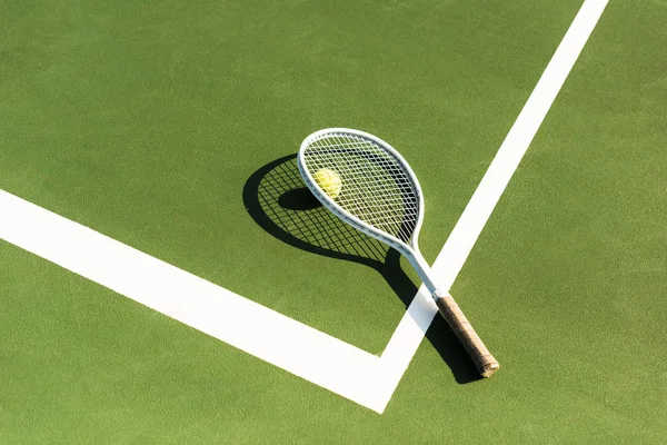 Close up view of tennis racket and ball lying on green tennis court — Stock Photo