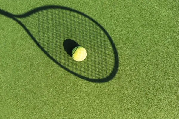 Top view of tennis ball and tennis racket shadow on green tennis court — Stock Photo