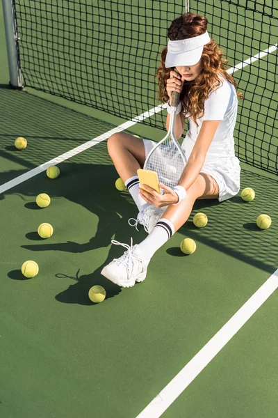 Stylish tennis player in white sportswear with equipment taking selfie on smartphone at net on tennis court — Stock Photo