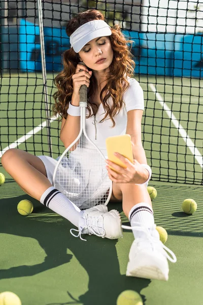 Sportive élégante en vêtements de sport blancs avec raquette de tennis prenant selfie sur smartphone au filet sur le court de tennis — Photo de stock