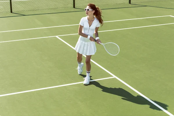 Side view of young attractive woman in white tennis uniform playing tennis on court — Stock Photo