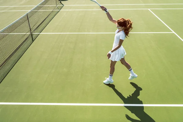 Seitenansicht einer jungen attraktiven Frau in weißer Tennisuniform, die Tennis auf dem Platz spielt — Stockfoto