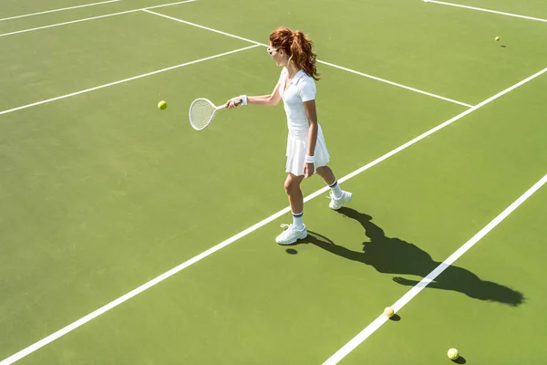 Vista laterale della giovane donna attraente in uniforme da tennis bianco che gioca a tennis sul campo — Foto stock