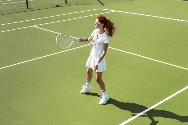 Joven jugadora de tenis en gafas de sol jugando tenis en la cancha - foto de stock