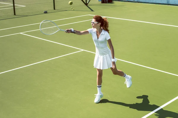 Young female tennis player in sunglasses playing tennis on court — Stock Photo