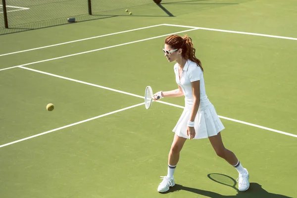 Young female tennis player in sunglasses playing tennis on court — Stock Photo