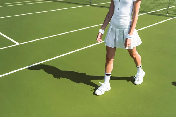 Cropped shot of female tennis player in white sportswear walking on tennis court — Stock Photo
