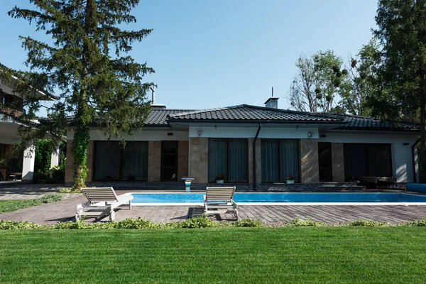 Vista de la casa moderna, junto a la piscina con tumbonas y césped verde - foto de stock
